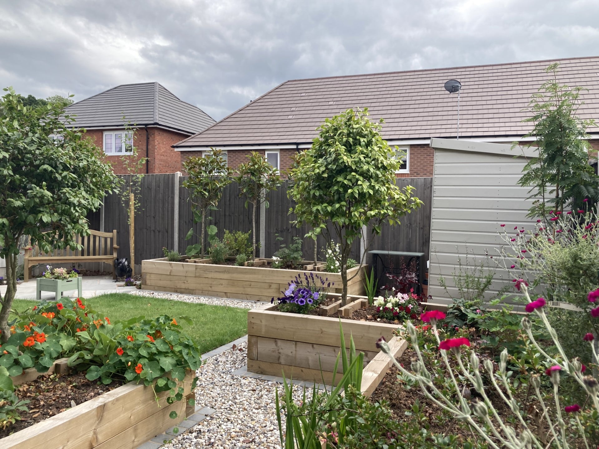 Cottage of Suburbia - After - finished garden shot with vibrant plants in raised beds and shed